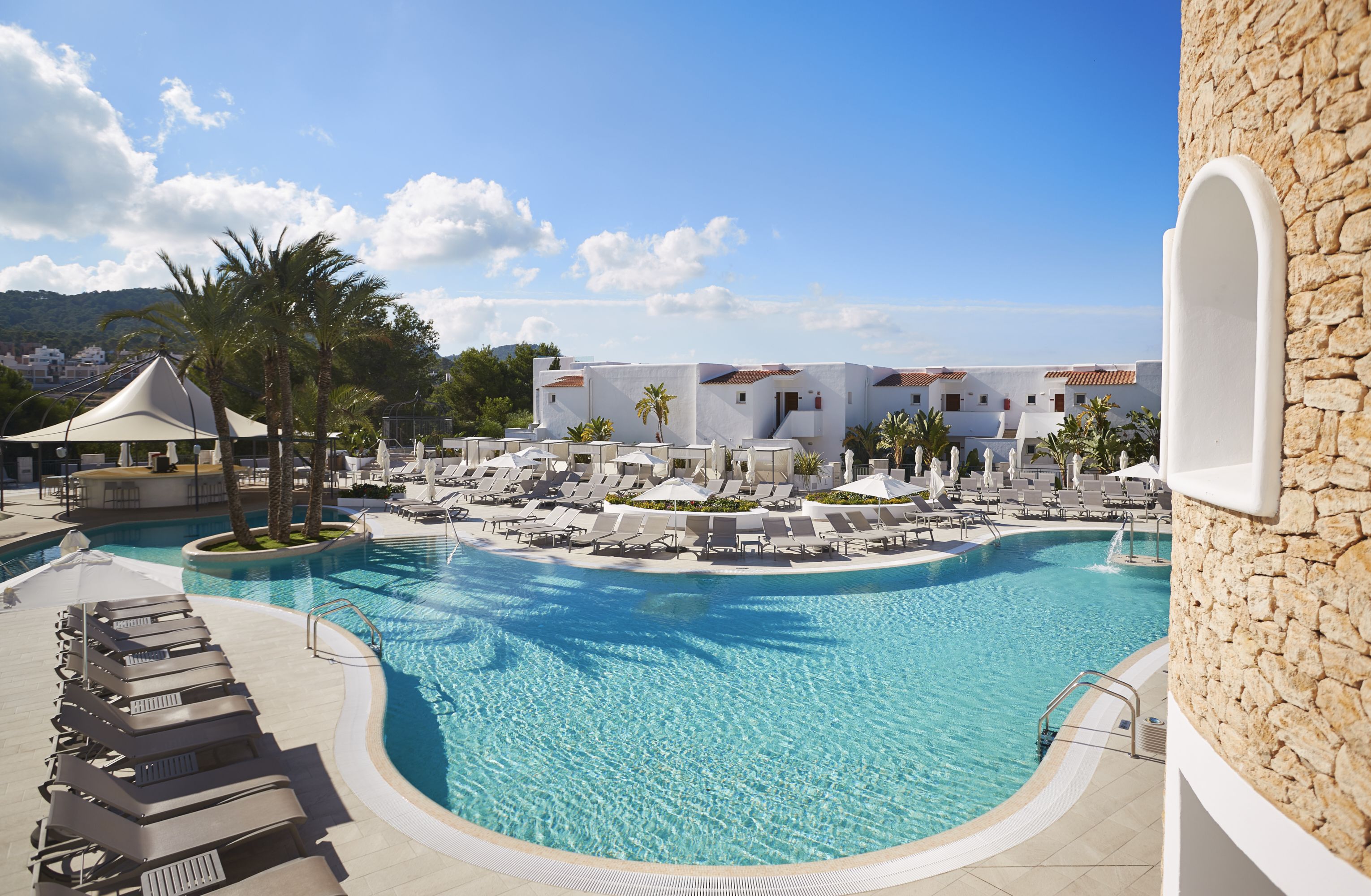 A resort pool area with lounge chairs, a covered seating area, and a view of the resort buildings.