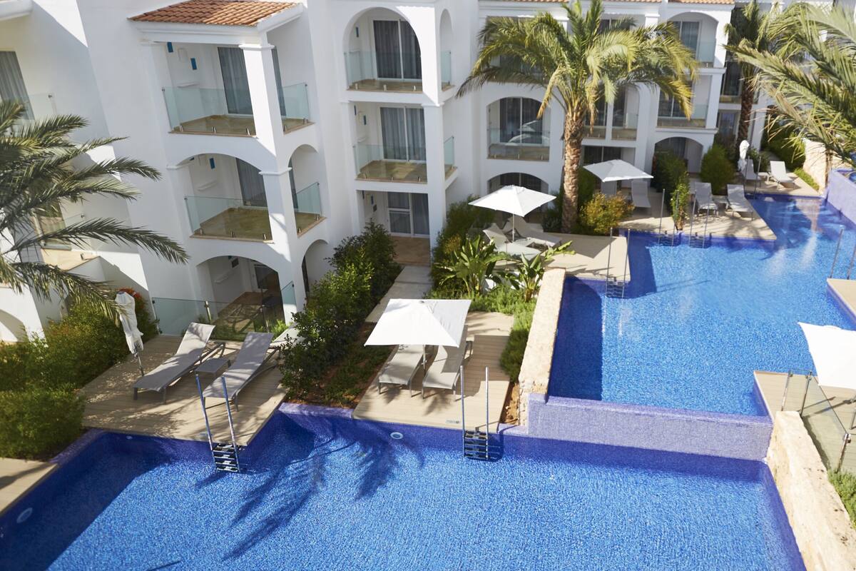 A resort with multiple swimming pools, white buildings, and palm trees.