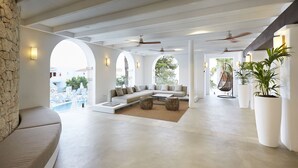 A spacious living area with a large sofa, a coffee table, and two side tables. There are ceiling fans, a stone wall, and potted plants. - Insotel Tarida Beach Resort & SPA - All inclusive (Sant Josep de sa Talaia)