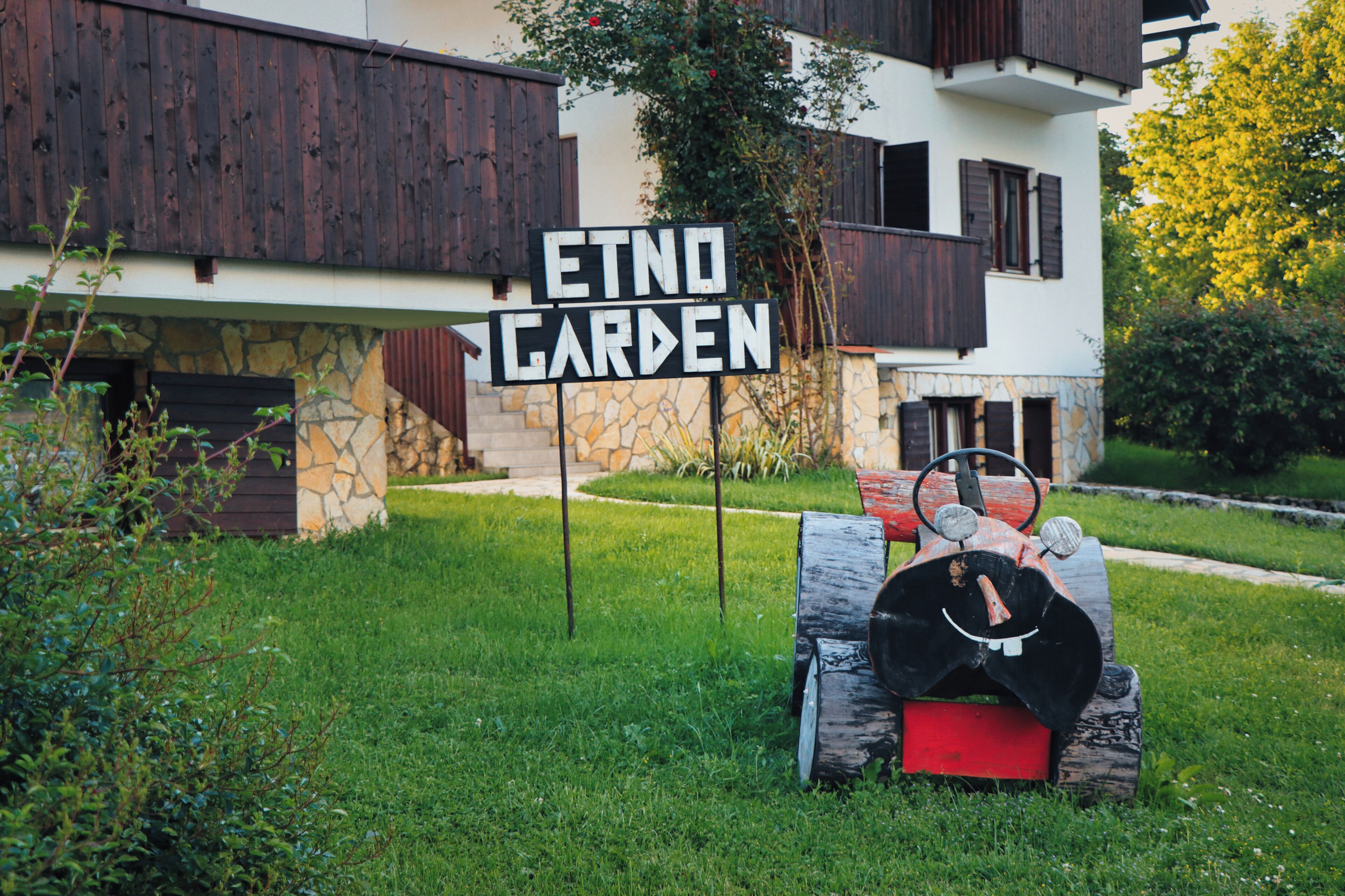 Un letrero que dice 'ETNO GARDEN' frente a un edificio con paredes de piedra y contraventanas de madera.