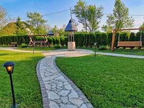 Un chemin de pierres mène à un belvédère situé dans un jardin bien entretenu, où se trouvent également une balançoire et un banc.