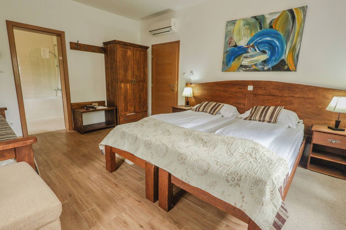A bedroom with a wooden bed, a nightstand, a bedside table, a wardrobe, and a shower.