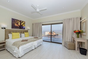 Una habitación de hotel moderna con una cama grande, ventilador de techo, balcón con mesa y sillas, y vista del paisaje.