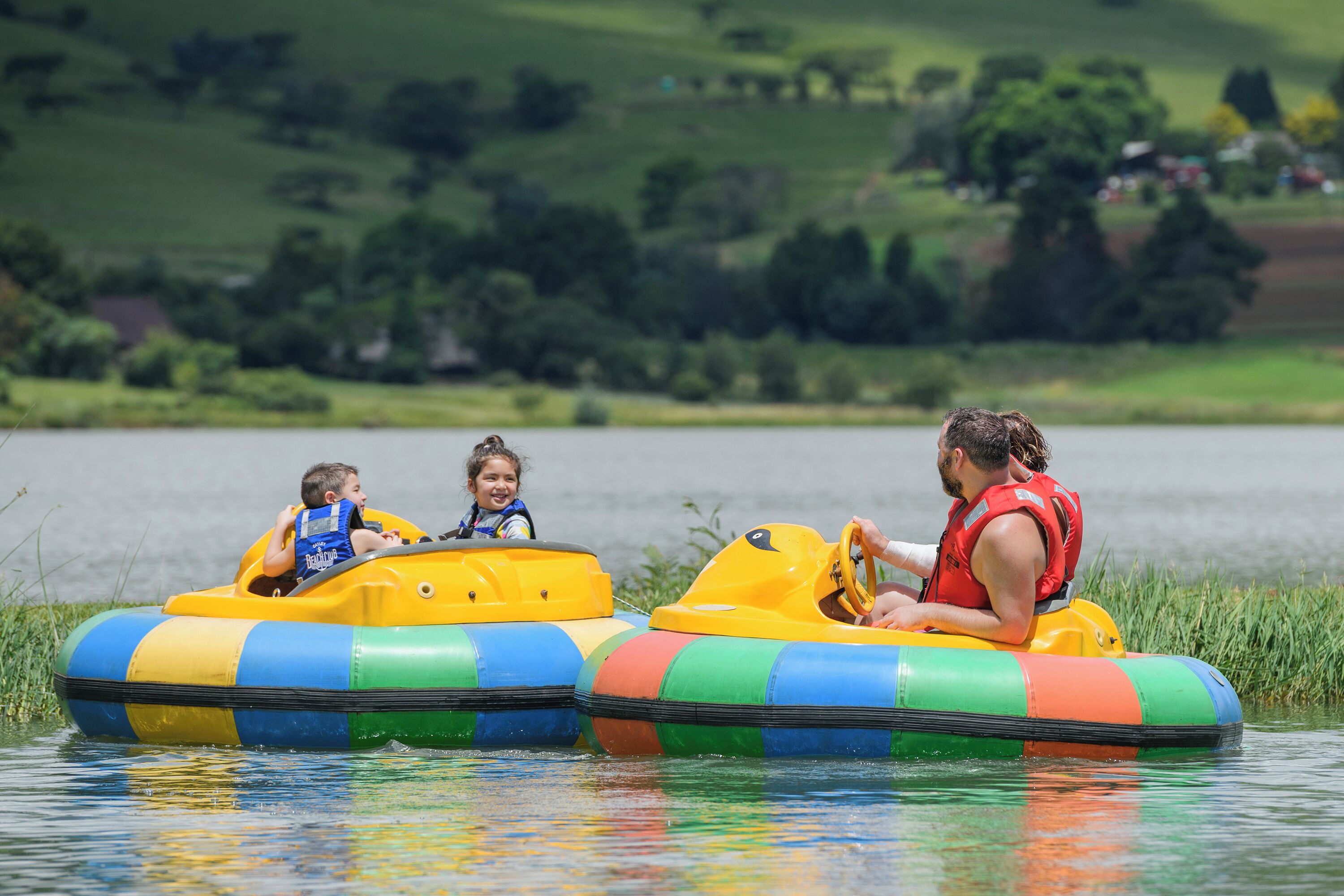 Two people in a yellow inflatable raft on a body of water with a grassy landscape in the background.