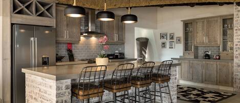 Una cocina moderna con una isla central, taburetes de bar y un refrigerador de acero inoxidable.