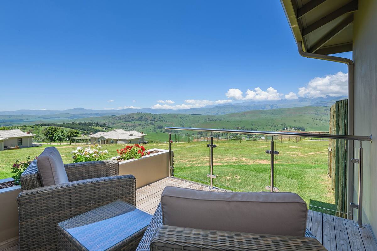 Un balcon agrémenté de meubles en osier, offrant une vue sur des collines ondoyantes et des montagnes lointaines.
