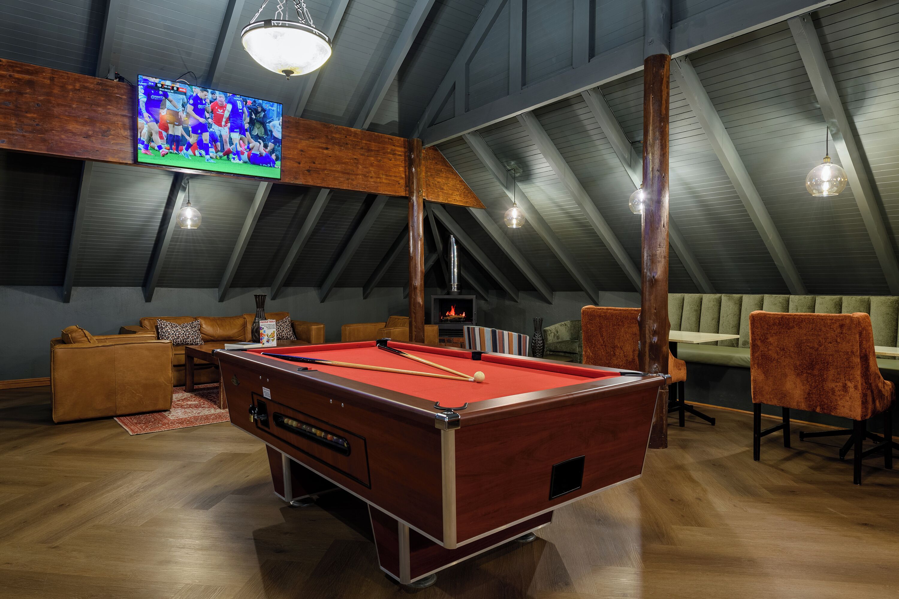 A pool table in a room with a high ceiling, a television, and seating.