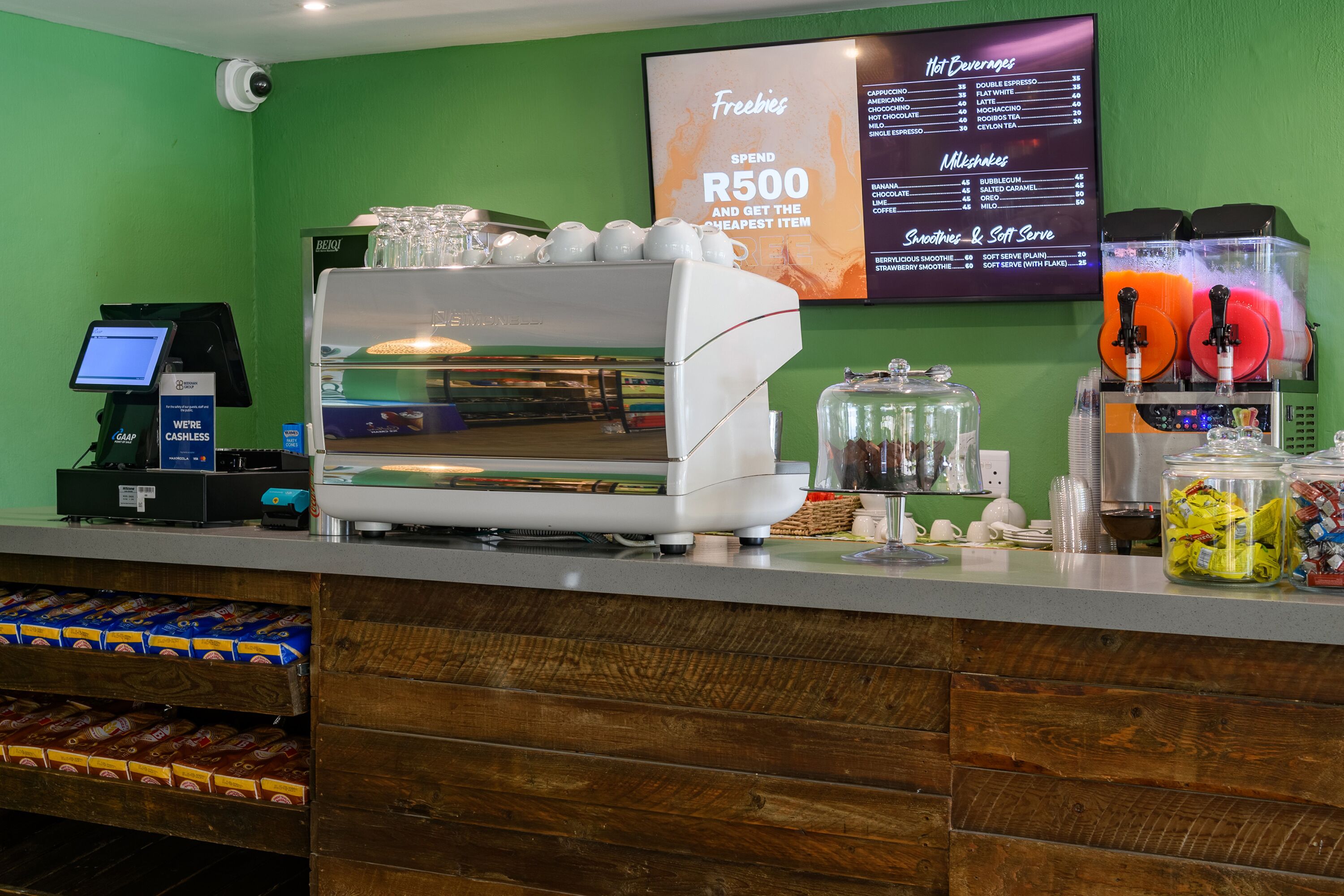Een toonbank bij een koffiebar met een koffieapparaat, een menubord en een pinapparaat.
