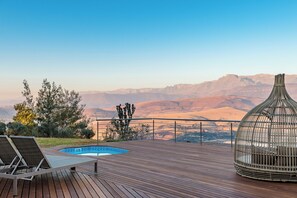 Una terraza de madera con piscina, sillas de descanso y una jaula de pájaros.