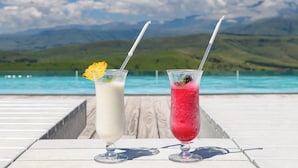 Dos bebidas sobre una mesa, con una piscina y montañas al fondo.