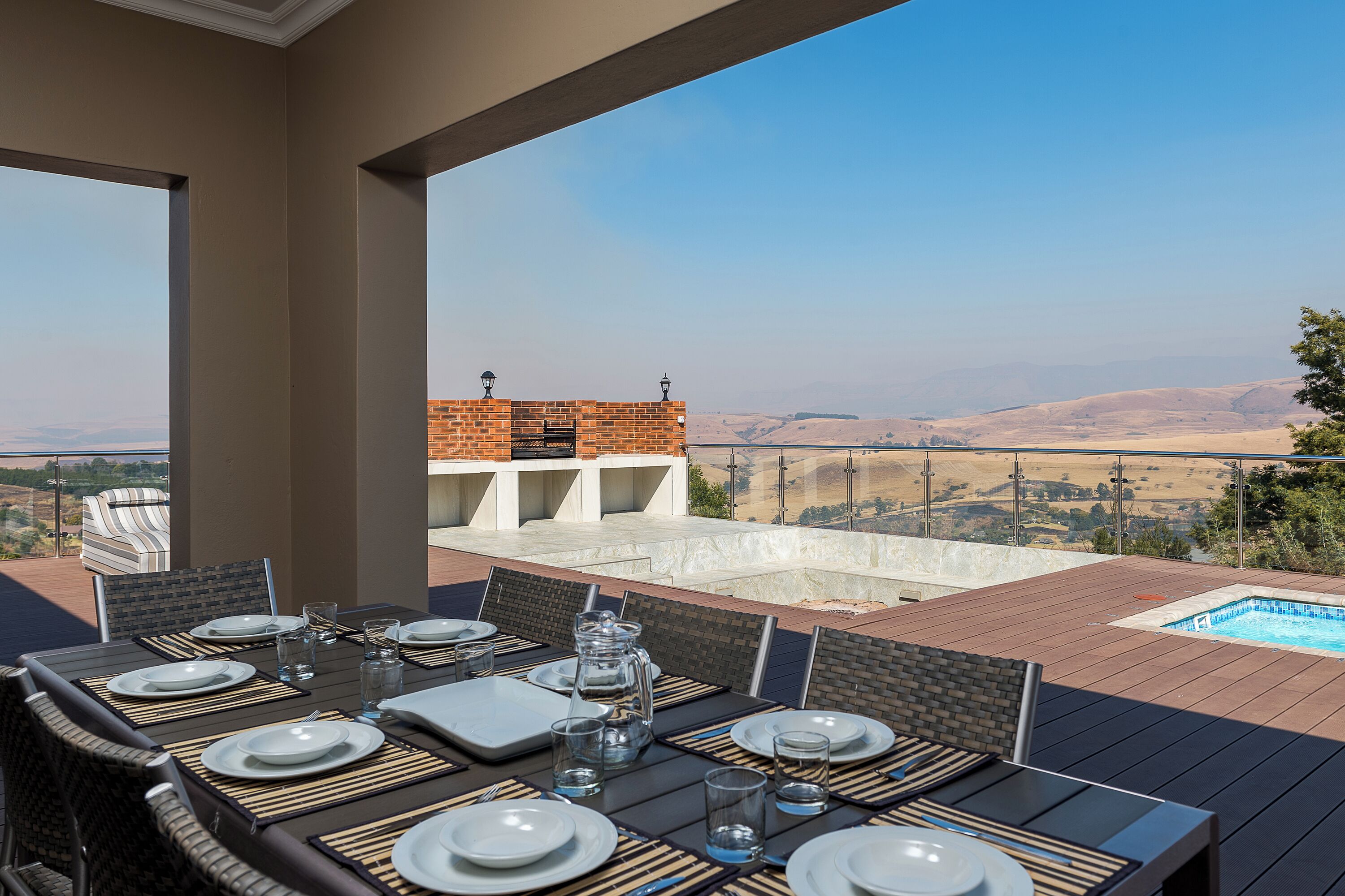 Un área de comedor al aire libre con vistas a una piscina y colinas distantes.
