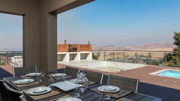 Un área de comedor al aire libre con vistas a una piscina y colinas distantes.