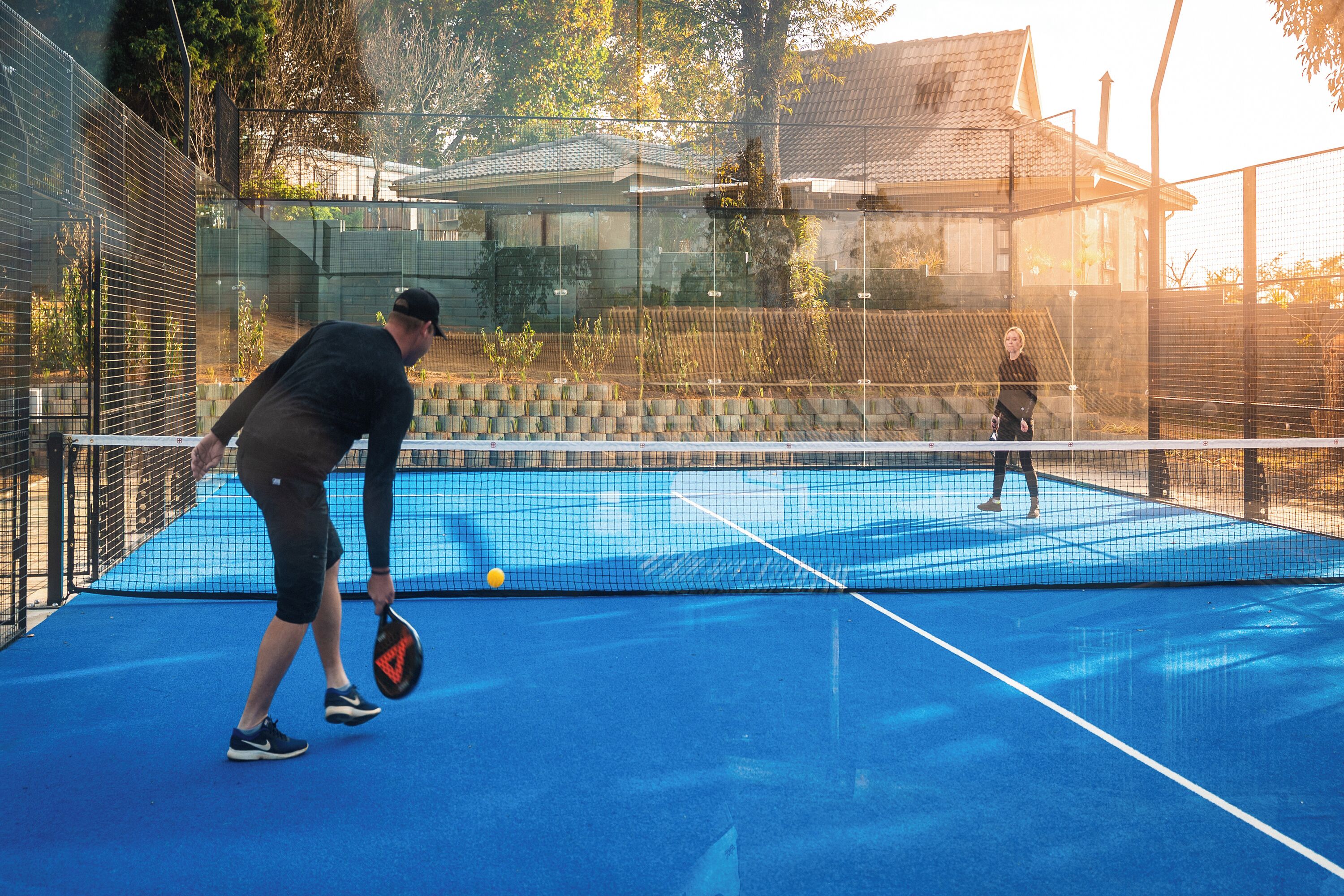 A tennis court with a net, a person holding a racket, and another person in the background.
