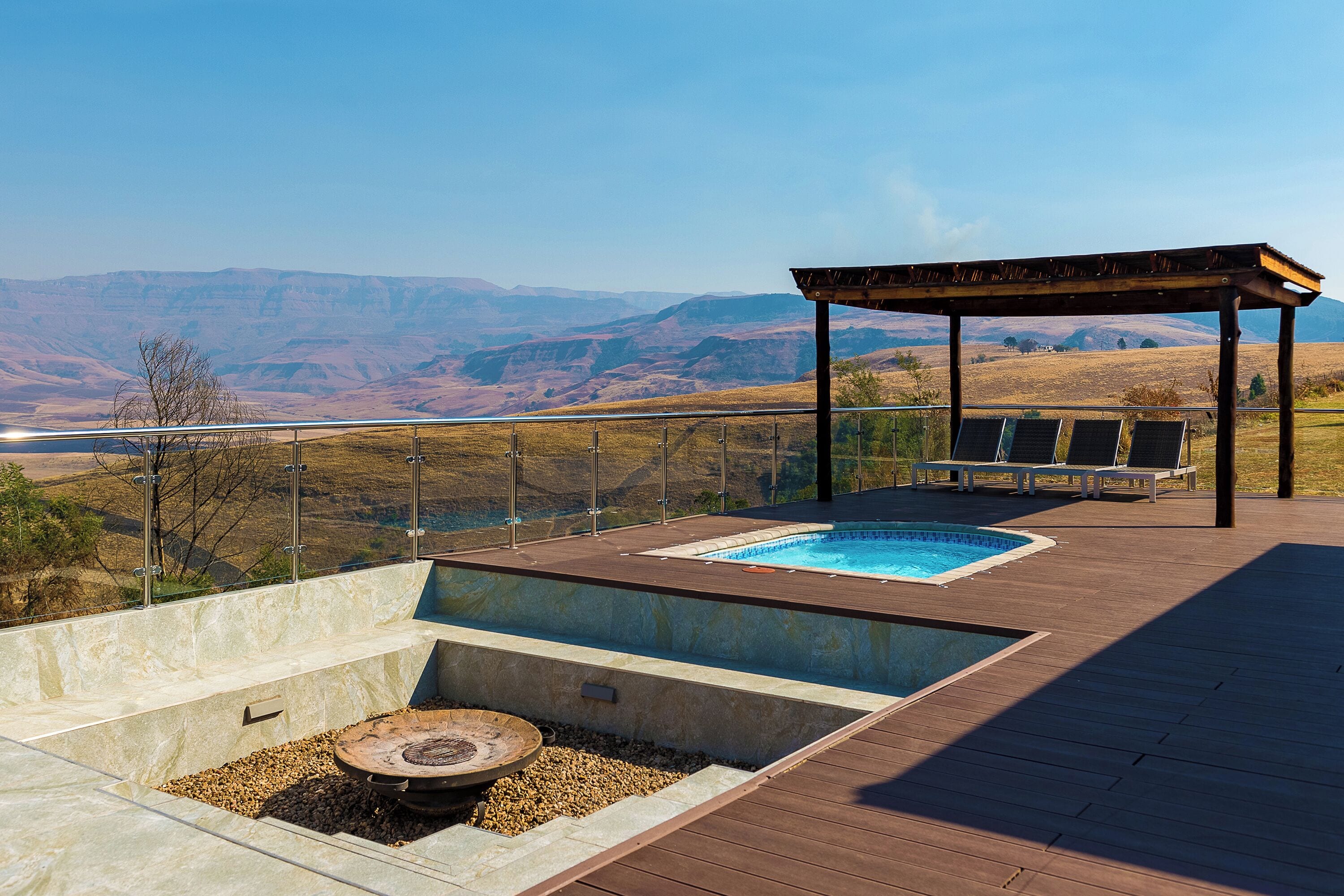 A pool area with a pergola and lounge chairs, surrounded by a scenic mountain view.