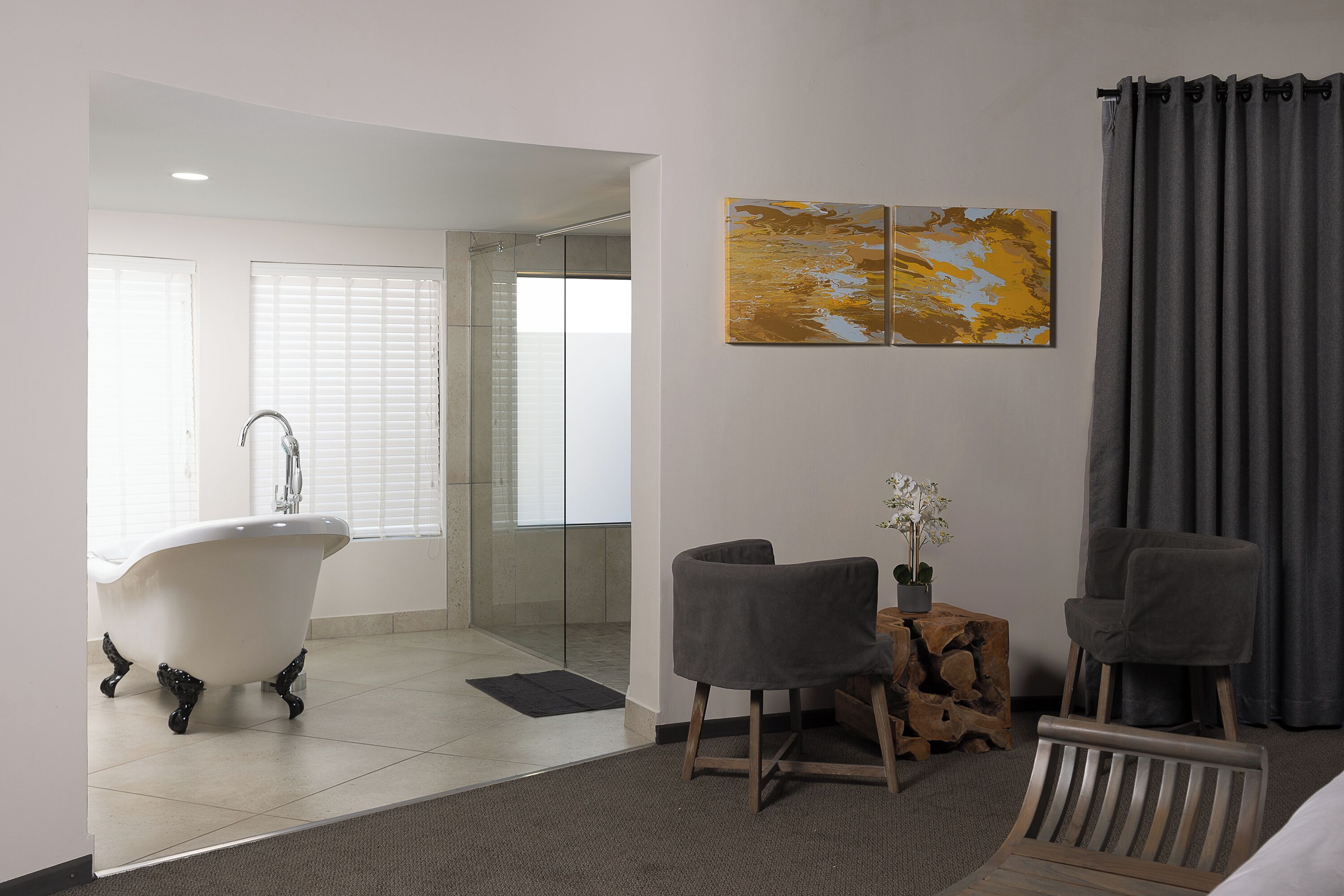 Un baño moderno con una bañera independiente, un box de ducha de vidrio y una zona de estar con dos sillones y una mesita.