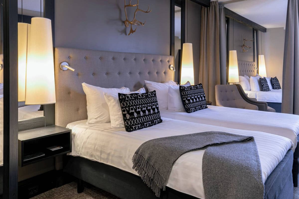 Une chambre d’hôtel avec un grand lit, des lampes de chevet, une chaise et une fenêtre.