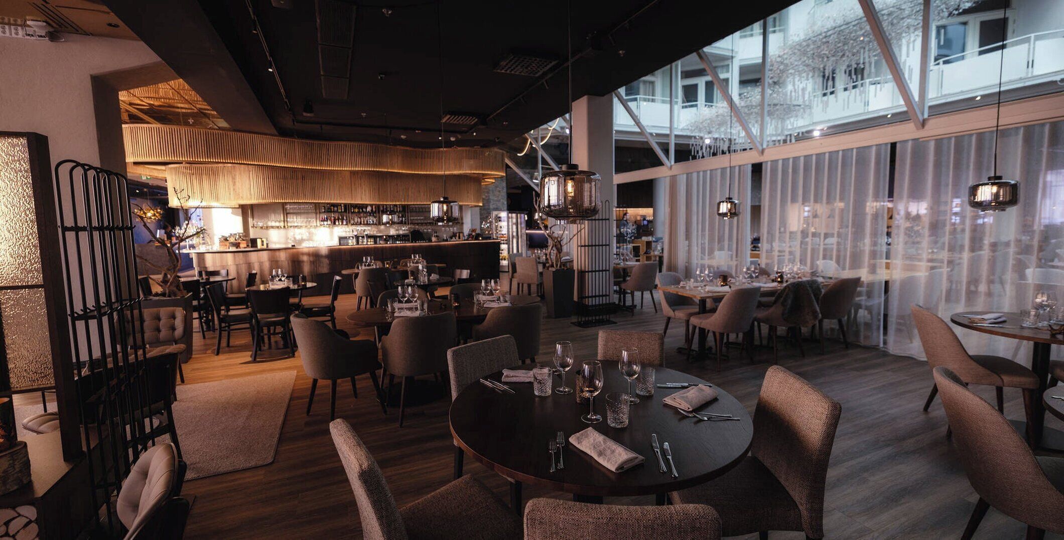 A modern restaurant with round tables, chairs, and a bar area.