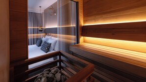 Una habitación de hotel moderna con un banco de madera, una chimenea de piedra y vistas a un dormitorio con cama y cortinas.