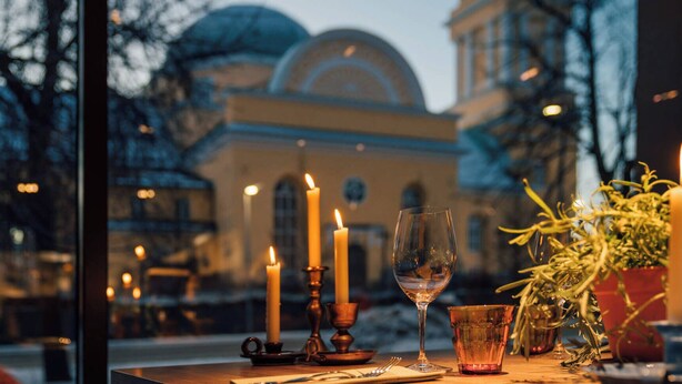 Una mesa con velas, una copa de vino y un vaso, con vistas a un edificio con cúpulas.