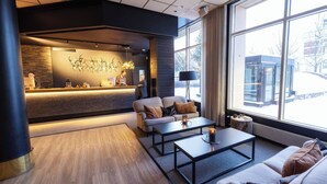 Un lobby moderno de hotel con mostrador de recepción, zona de estar y grandes ventanales con vistas a la ciudad.
