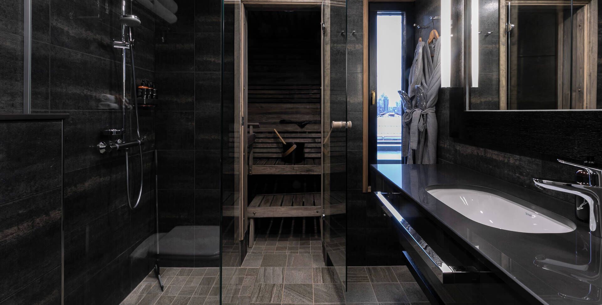 A modern bathroom with a glass-enclosed shower, a large sink, and a view of the city through a door.