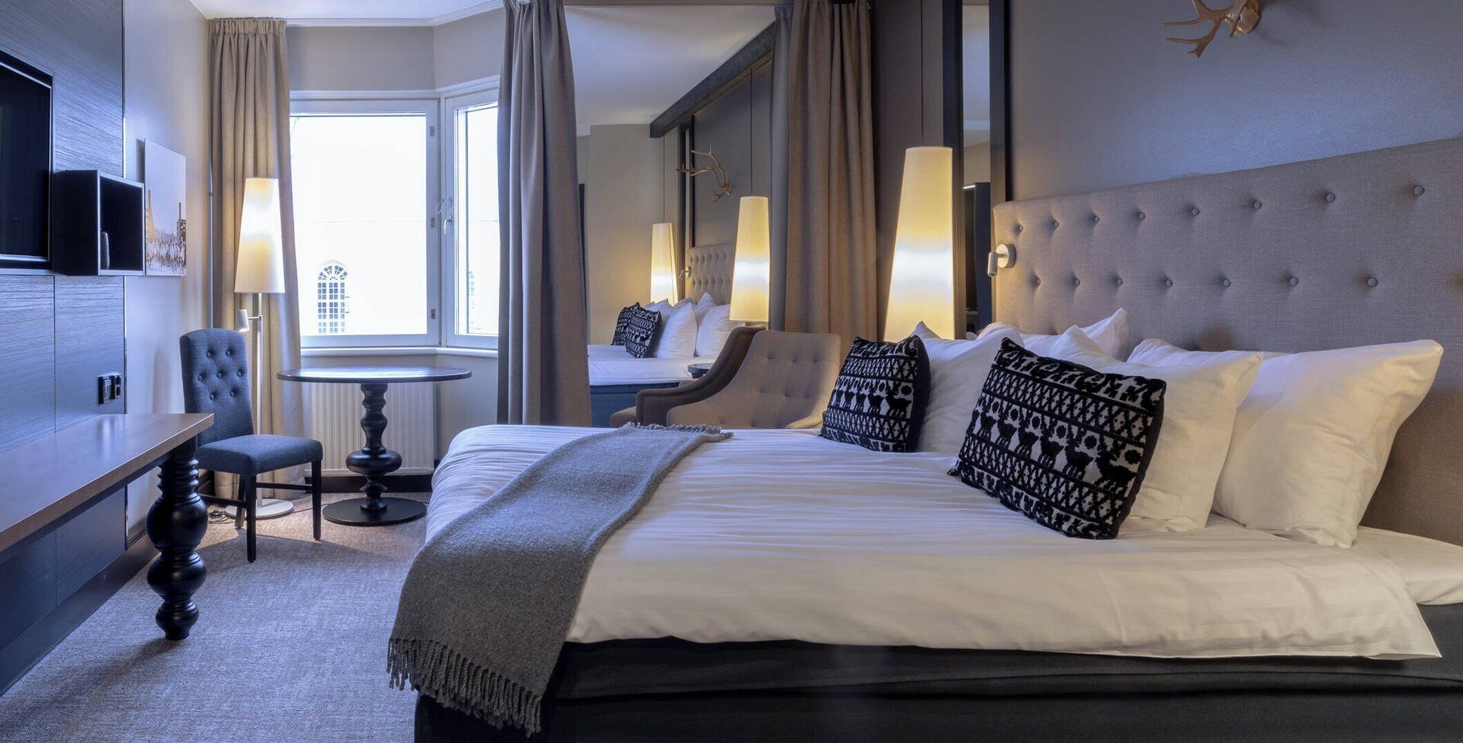 A hotel room with a large bed, a desk, a chair, a round table, and a television.