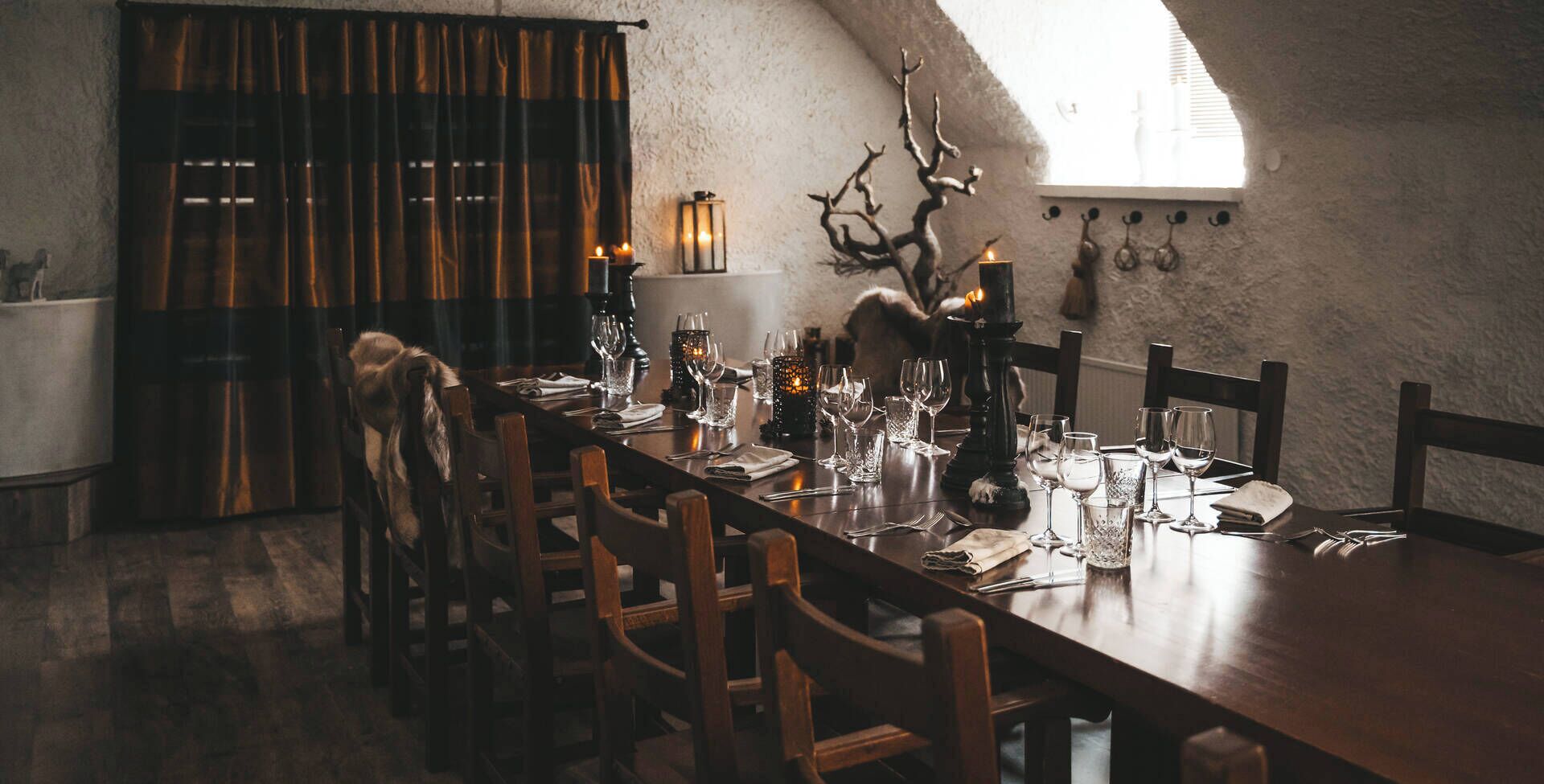 Un coin repas avec une longue table dressée pour le repas, des chaises en bois, un lustre et une tête de cerf décorative accrochée au mur.