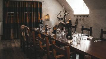 Un coin repas avec une longue table dressée pour le repas, des chaises en bois, un lustre et une tête de cerf décorative accrochée au mur.