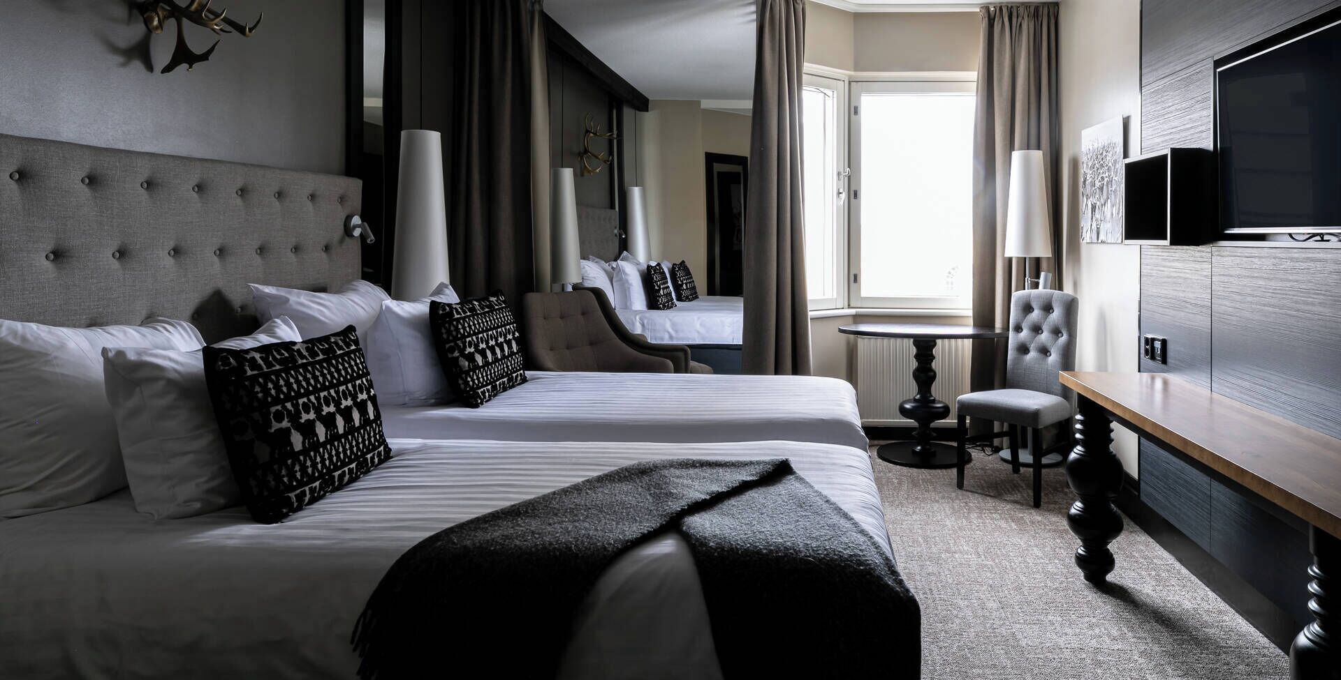 Quarto de hotel com duas camas, televisão, escrivaninha e janela com cortinas.