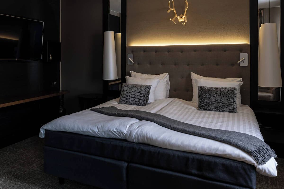 Une chambre d’hôtel moderne dotée d’un grand lit, de lampes de chevet, d’un téléviseur à écran plat et d’une table de chevet en bois foncé.