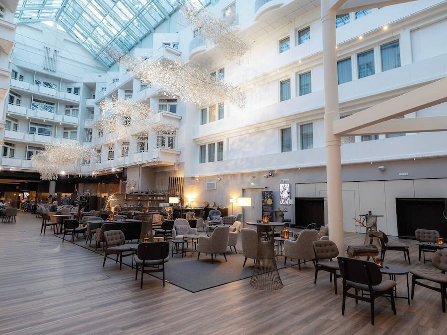 A spacious hotel lobby with multiple seating areas, a bar, and a high ceiling with natural light.