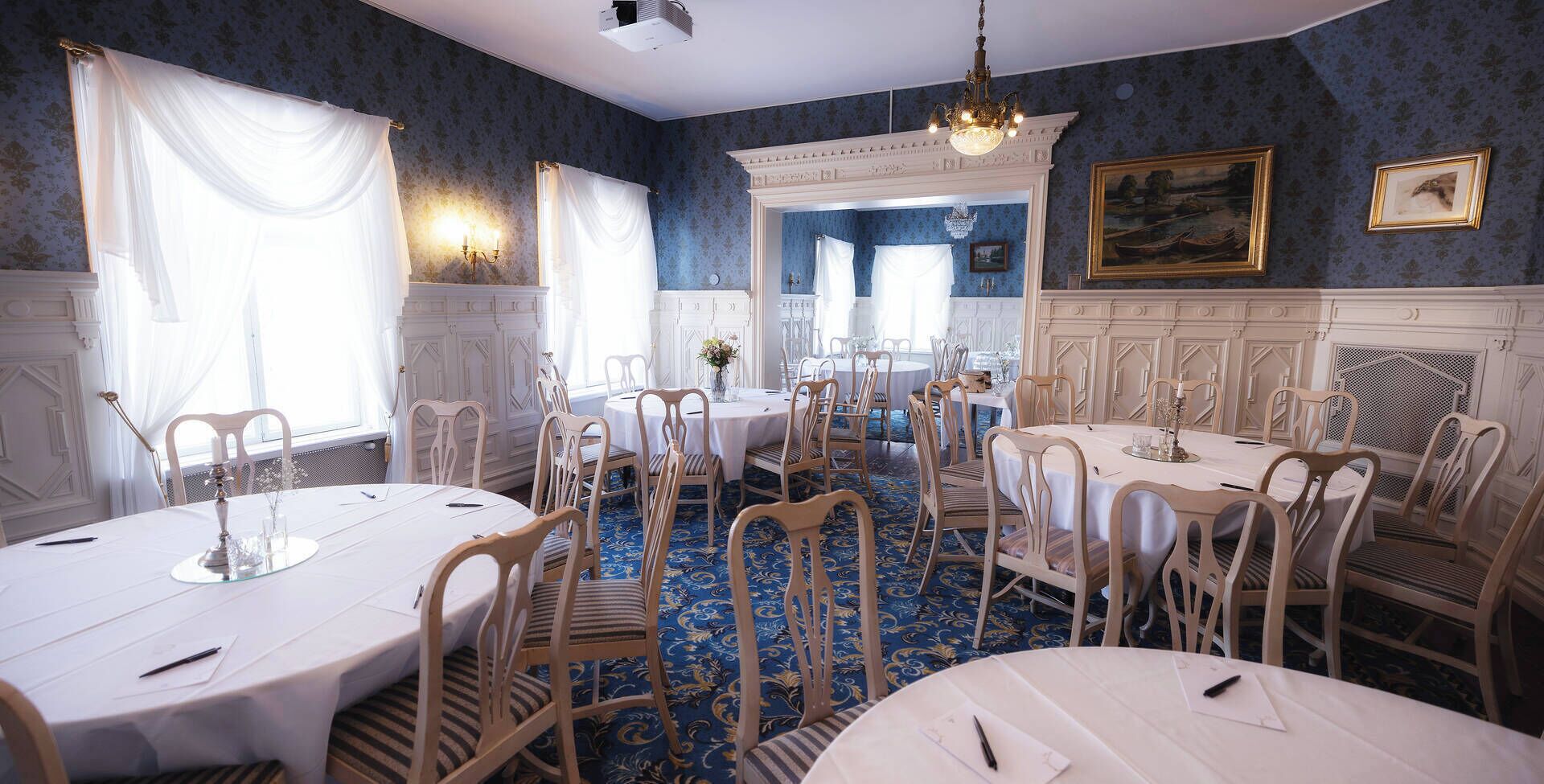 Un comedor formal con mesas redondas, sillas blancas y alfombra con motivos azules.