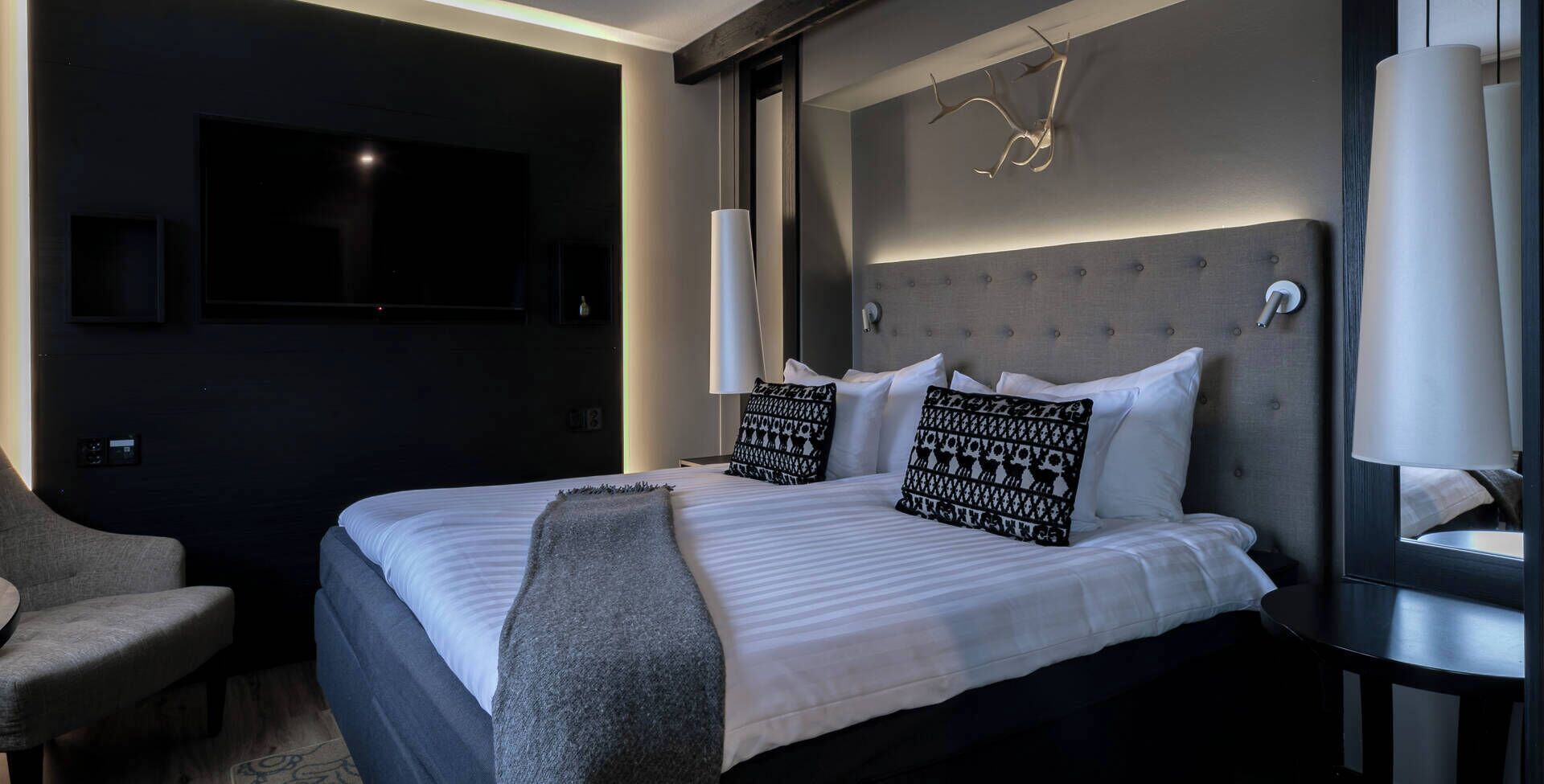 A modern hotel room with a large bed, a TV, a desk, and a chair.