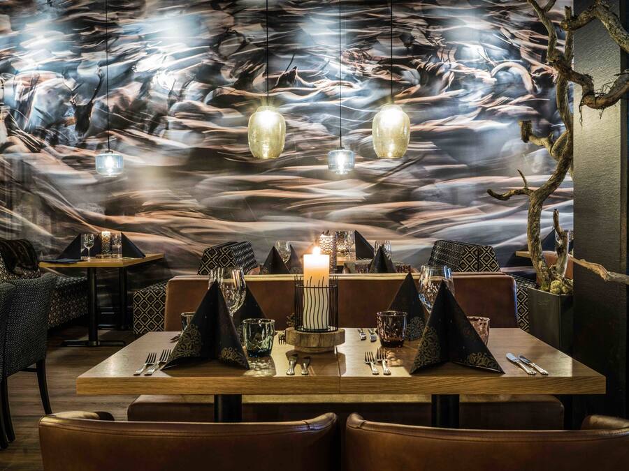A restaurant with a modern interior, featuring a dining table set with a candle, patterned napkins, and a unique wall mural.