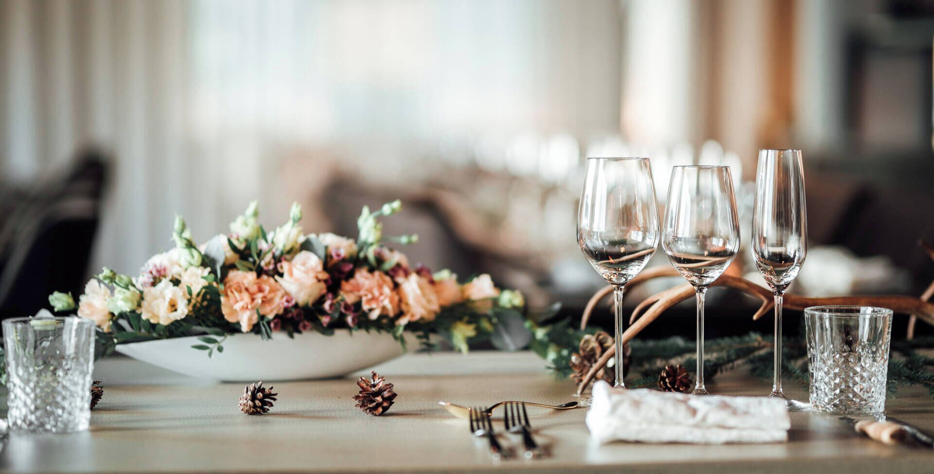 Una mesa servida con copas de vino, un centro de mesa floral y piñas.