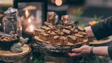 A table with a wooden platter holding dessert slices, surrounded by candles, a salt shaker, and Christmas decorations.