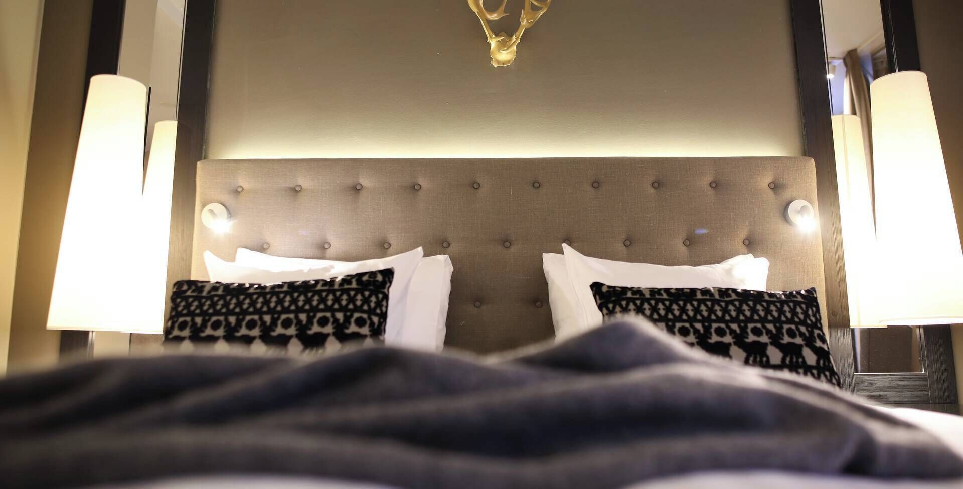 A hotel room with a tufted headboard, two bedside lamps, and patterned pillows.