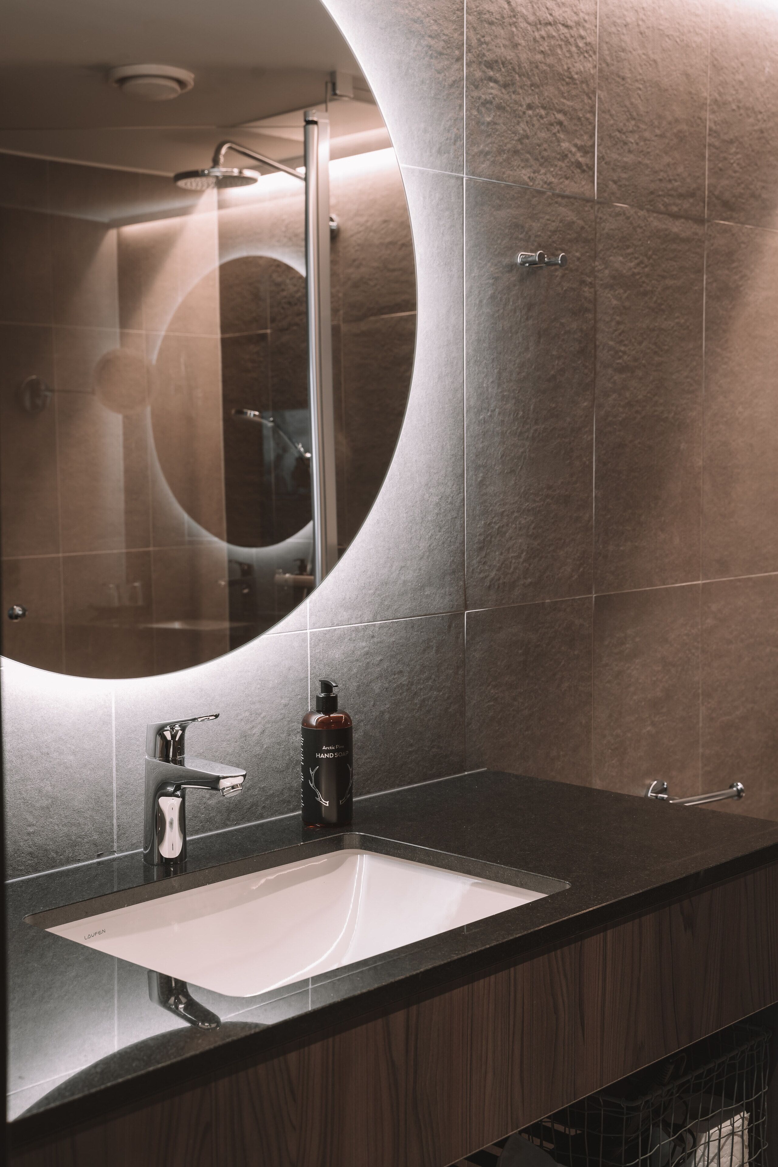 A modern bathroom with a curved mirror, a white sink, and a dark countertop.