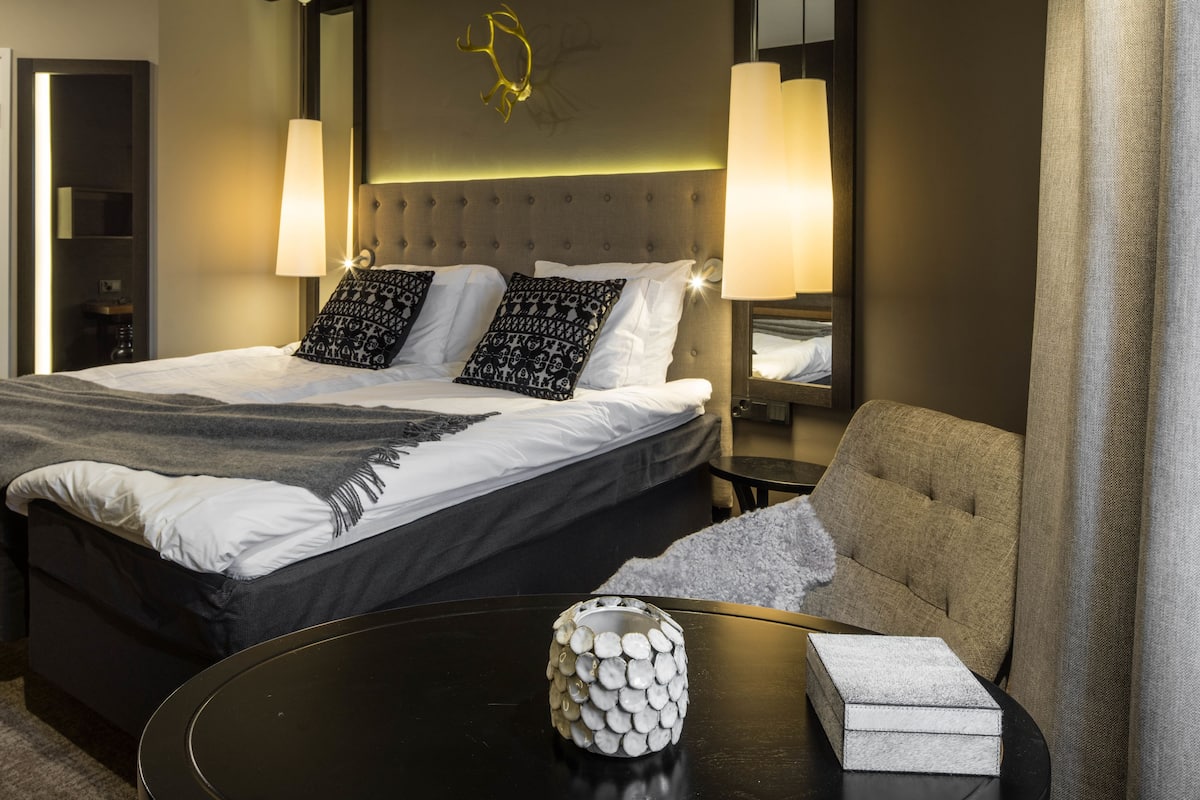 Une chambre d’hôtel avec un grand lit, deux lampes de chevet, une table ronde ornée d’un vase décoratif et une chaise.