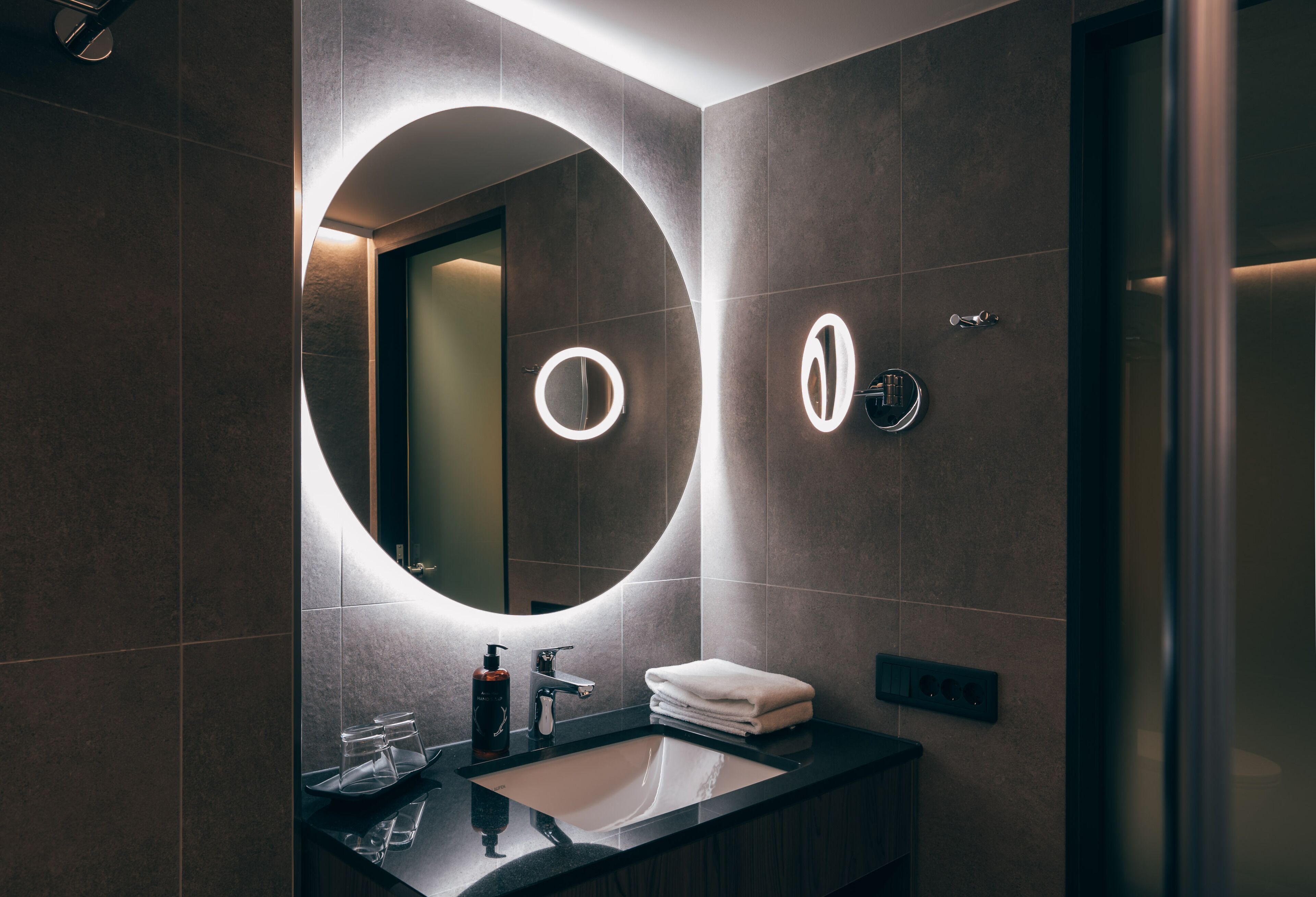 A modern bathroom with a large mirror, a sink, and a towel rack.