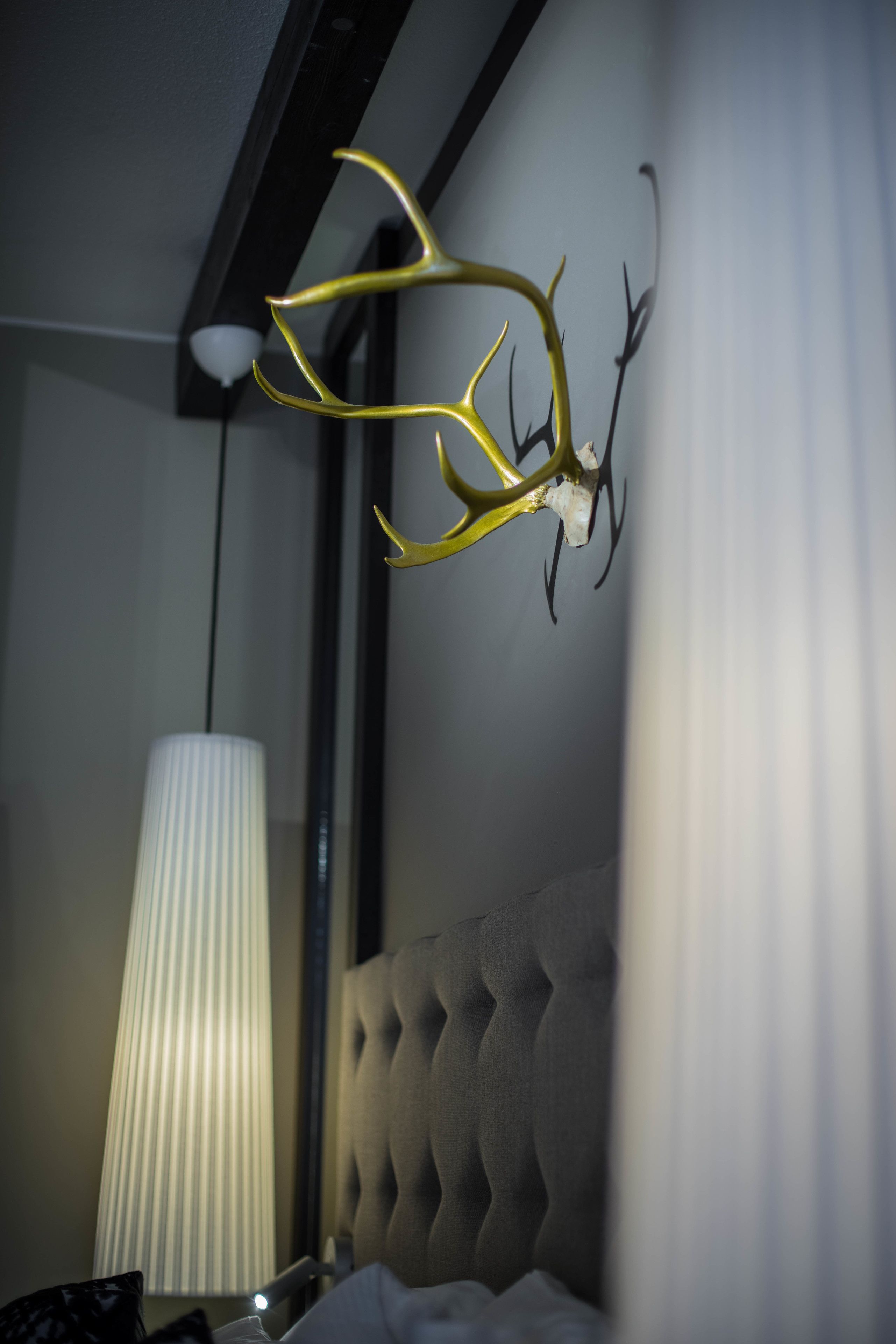 A room with a tufted headboard, a wall-mounted light fixture, and a decorative antler piece.