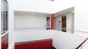 L’intérieur d’un hôtel avec un mur d’accent rouge, un plafond blanc et une rambarde en verre.