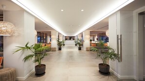Un hall d’hôtel moderne avec un chemin central, des plantes en pot et un comptoir d’accueil en arrière-plan.