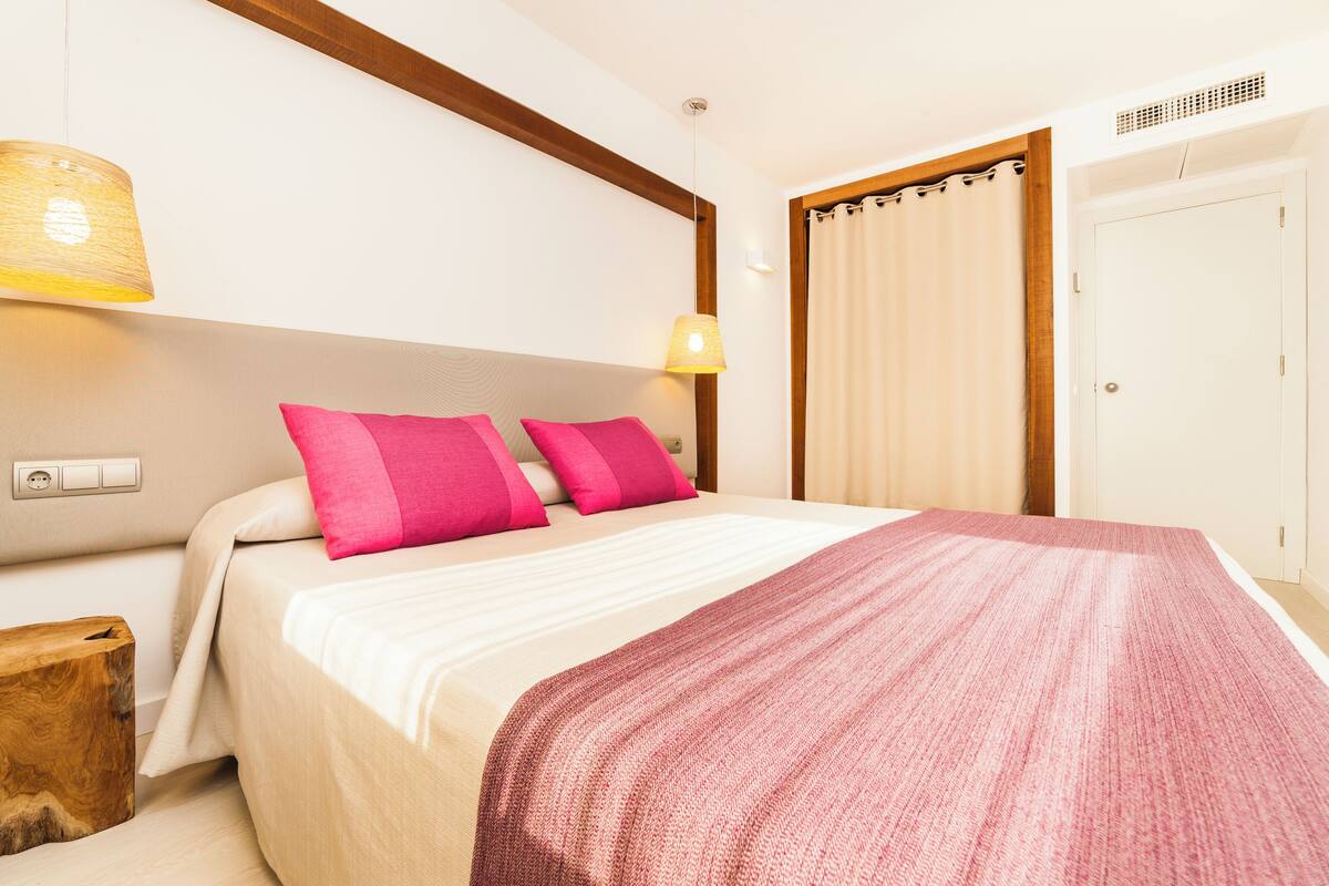 A hotel room with a bed, a wooden headboard, a bedside lamp, a nightstand, and a wardrobe.