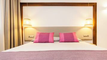 Een netjes opgemaakt bed met twee roze kussens, een wit hoofdbord en twee wandlampen.