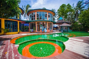 Et resort med en stor swimmingpool, en cirkelformet bygning med mange vinduer og en pavillon.