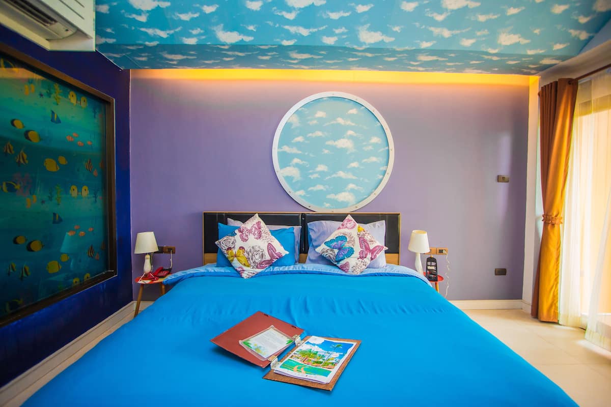 A room with a bed, a round mirror, and a window with curtains.