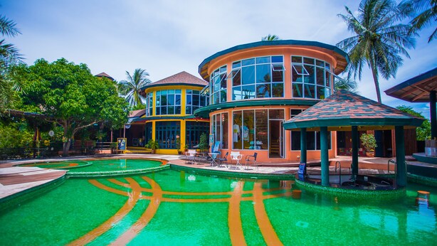 A resort with a large pool, multiple buildings, and palm trees. - Vartika Adventure Retreatic Resort (Prachuap Khiri Khan)