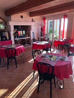 A dining area with multiple tables covered in red tablecloths, black chairs, and a fireplace with decorative items.
