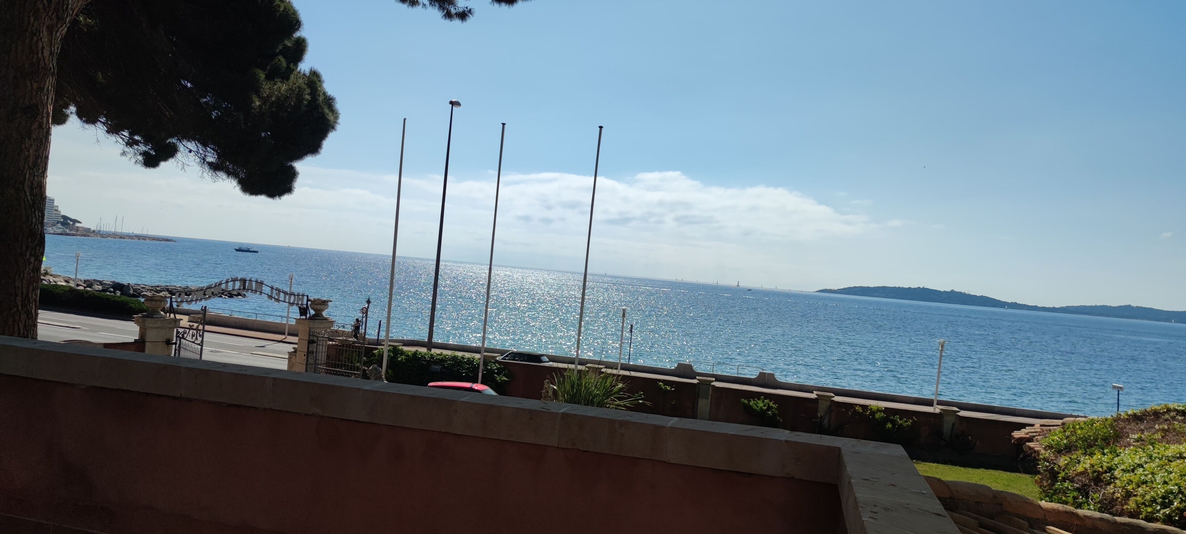 A coastal view with a clear sky, a paved walkway, and a distant shoreline.